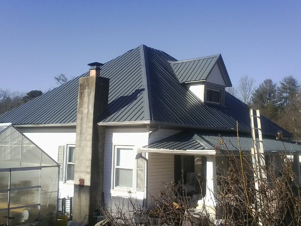 Dark blue standing seam metal roof on a white farmhouse with dormer — Slate & Tile Roof Repair by Roofing Brothers in Moneta