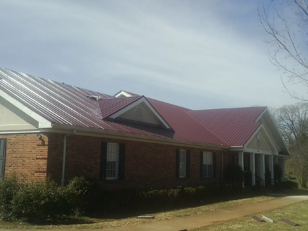 Red metal roof with gabled entries on a long brick building, from a Hail Damage Roof Repair job in Moneta