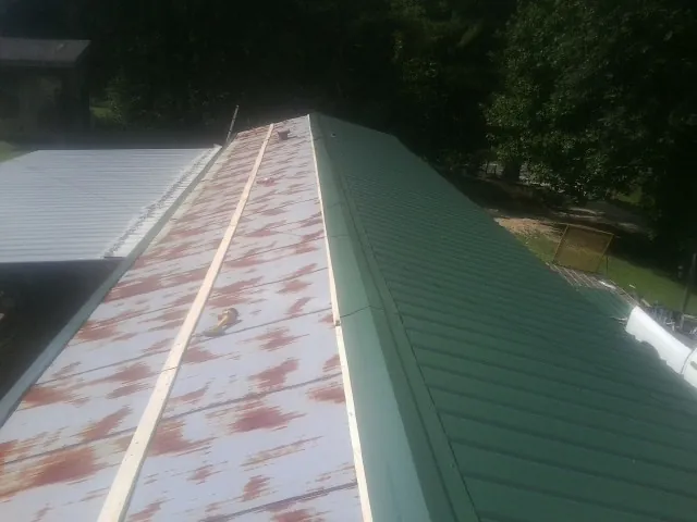Old rusted panels beside newly installed green metal roofing — Wind Damage Roof Repair by Roofing Brothers in Moneta