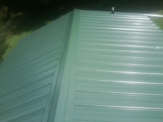 New green metal panels meeting at the ridge of a roof — Flat Roof Repair work by our crew in Moneta