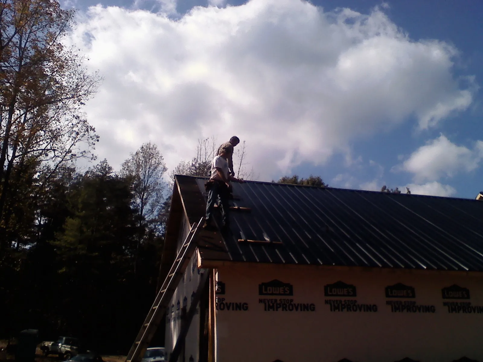 Roofer fastening dark metal panels high against a cloudy sky, from a Roof Inspection job in Moneta