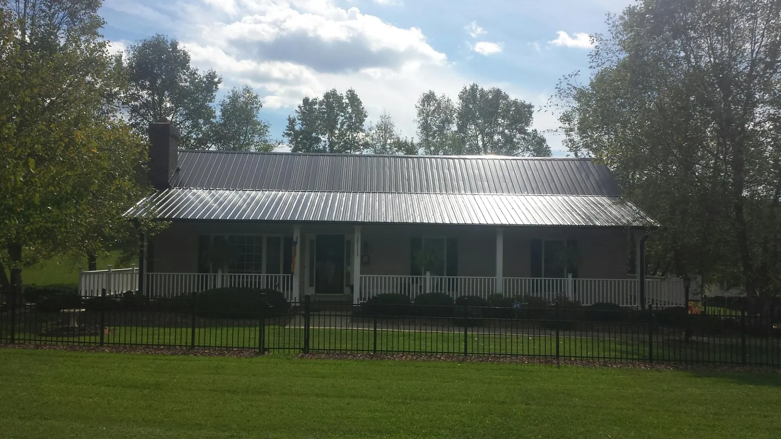 Gray metal roof on a brick ranch with a full width front porch — Gutter Guard Installation work by our crew in Moneta