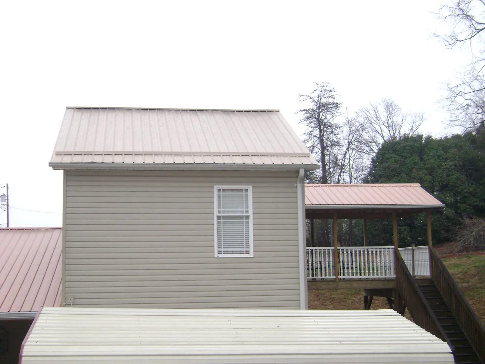 Tan metal roofs on a two story addition and attached porch, from a Roof Replacement job in Moneta